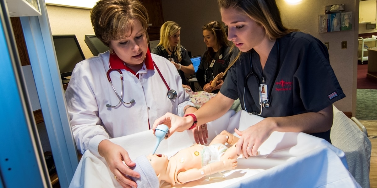 A Northwestern professor watches as a nursing student cares for a patient simulator.