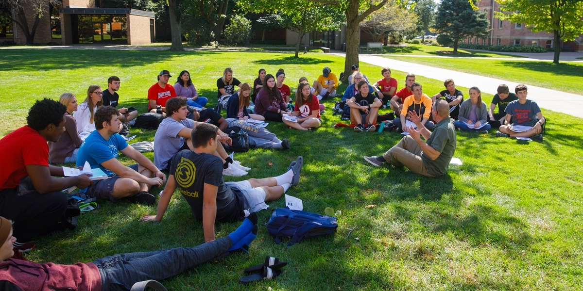 A professor teaches a theology class outside on a pleasant fall day.