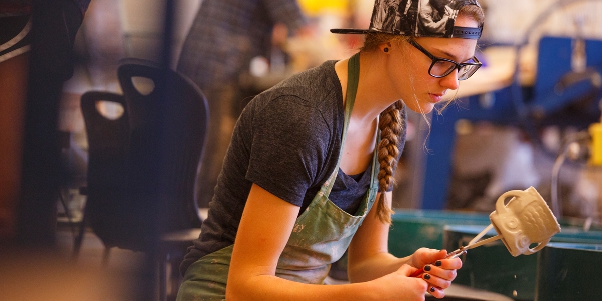A Northwestern student dips a clay pot into glaze.